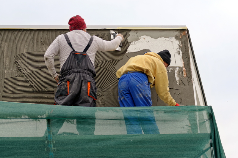 19 - Two construction workers applying plaster or mortar to an exterior wall from a scaffold